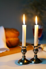 vertical photo Traditional challah bread with wine and glowing candles on dark background. Shabbat Shalom