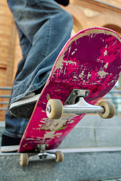 Low angle view of skateboarder balancing on pink skateboard. Close up of underside of deck and wheels of skateboard on stairs at city street