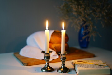 Shabbat or Sabbath kiddush ceremony composition with a traditional sweet fresh loaf of challah bread, glass of red kosher wine and candles on a vintage wood table with copy space