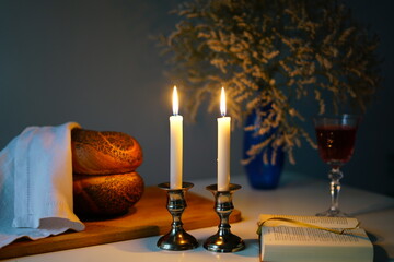 Traditional challah bread with wine and glowing candles on dark background. Shabbat Shalom