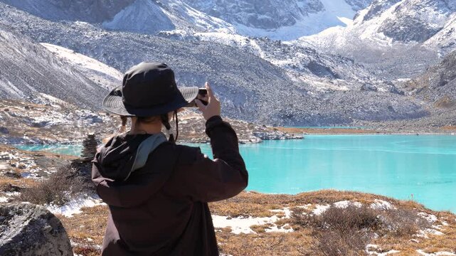 Woman hiker captures stunning images of turquoise lake nestled high in mountains. Snow capped rocks. Hiking trip. Active type recreation. Enjoying view. Capture moment. Share photo on social network