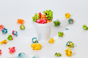 Colorful popcorn in a foam cup with some scattered around. Clean white background.