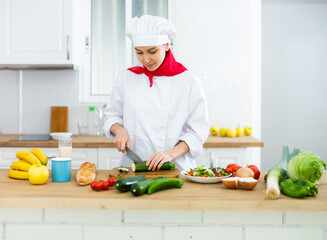 Portrait of positive woman chef cutting vegetables for salad