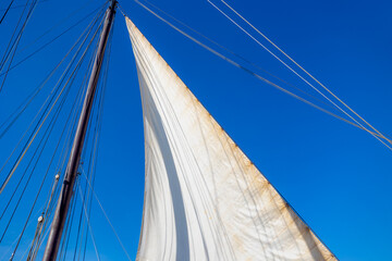Obraz premium Ocean liner or Sea sailing ship concept, Selective focus of white boat canvas with rops on spar, Sailcloth of sailboat with mainmast and boat hoist rope to spread the sails with blue sky as background