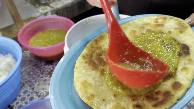 Hand dipping a freshly cooked huarache into a bucket of creamy sauce at a Mexican street food stand