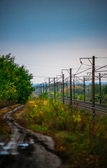 Railway road at autumn evening with autumn colors.Railroad near the forest with powerlines over the trees.Clouds in the sky,photography in the rainy weather .Landscape photo with train on the rails