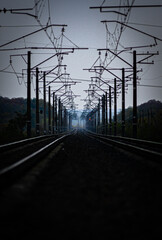 Railway road at autumn evening with autumn colors.Railroad near the forest with powerlines over the trees.Clouds in the sky,photography in the rainy weather .Landscape photo with train on the rails