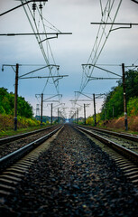 Railway road at autumn evening with autumn colors.Railroad near the forest with powerlines over the trees.Clouds in the sky,photography in the rainy weather .Landscape photo with train on the rails