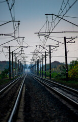 Obraz premium Railway road at autumn evening with autumn colors.Railroad near the forest with powerlines over the trees.Clouds in the sky,photography in the rainy weather .Landscape photo with train on the rails