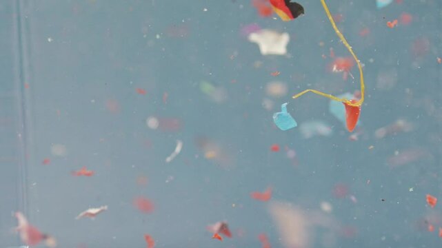 Microplastic particles swirl in water in slow motion, showcasing pollution in a lab sample and highlighting environmental waste issues.