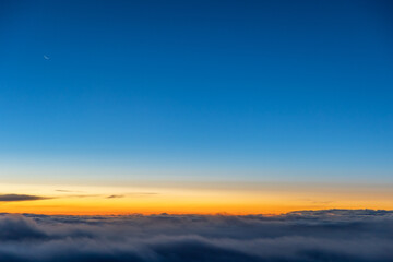 Aerial cockpit view of moonrise, crescent moon in dawn sky above clouds