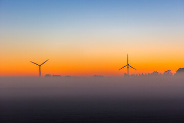 Two wind turbines, wind mills, generators at orange sunrise morning in rural Holland, Netherlands