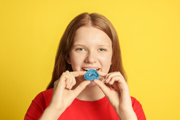 Teenage girl eating tasty gummy candy on yellow background