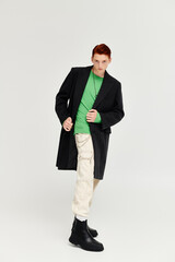 A young man with vibrant red hair models an elegant winter coat in a modern studio environment.