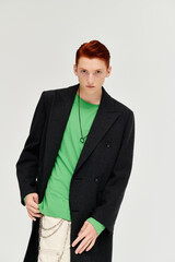 Fototapeta premium A handsome young man with red hair models an elegant winter coat in a vibrant studio, exuding style.