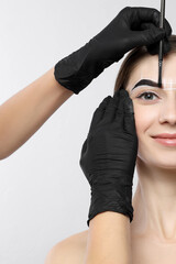 Young woman undergoing henna eyebrows dyeing procedure on light background, closeup