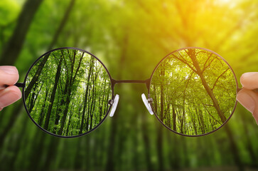 Woman holding glasses against in forest, closeup. View through lenses more clear. Vision correction