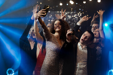 a group of people celebrate and take selfies, smiling and enjoying the moment in bright lights and a festive atmosphere. Everyone is dressed in evening clothes, the surroundings are decorated with lig