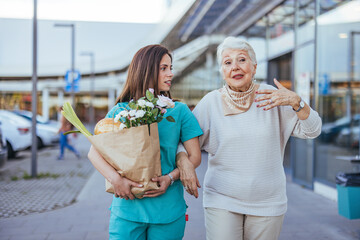 Young Caregiver Assisting Elderly Woman with Shopping Outdoors