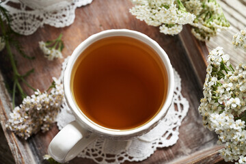 A white cup of herbal tea with fresh yarrow or Achillea millefolium flowers