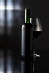 Glass and bottle of red wine on a black reflective background.