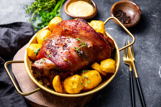 Baked pork knuckle with potatoes and cheese sauce on the table