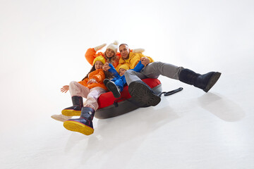 Happy family, mother, father and two kids, dressed in bright warm winter jackets, sliding in snow...