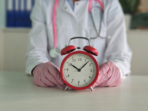 Red alarm clock standing on doctor table in clinic