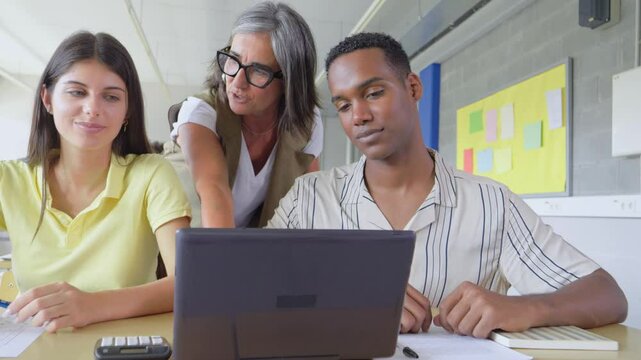 Diverse teenage students working as a team in class with a laptop and a teacher advising them