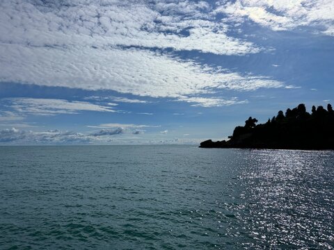 Sea glittering blue water, cloudy sky and rocky coast. 