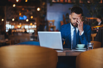 Obraz premium Stressed Businessman Working in a Cafe with Laptop and Coffee