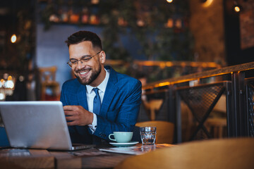 Smiling Businessman Working on Laptop in Modern Cafe