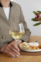 A glass of white wine in your hand against the background of a cheese plate with snacks and nuts