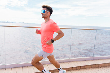 A Man Runs Along a Scenic Boardwalk by the Water During a Bright and Sunny Day, Enjoying His Outdoor Exercise Routine