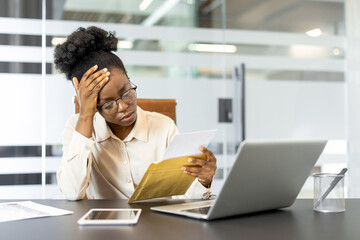 African American businesswoman looks stressed while checking documents in office. She uses a...