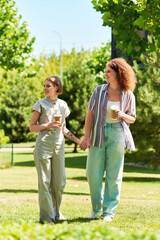 Fototapeta premium Two friends stroll through a vibrant park, sharing laughter and drinks under the sun.