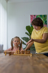 Happy granddaughter and her grandmother play chess at the table, creating sweet family memories
