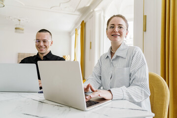 Two Professionals Working Collaboratively at a Bright and Modern Office Space With Large Windows and Yellow Curtains