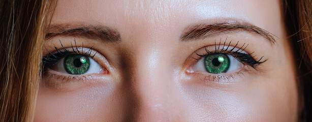 Close-up of a woman’s green eyes with detailed lashes and natural makeup, capturing clarity and intensity in her gaze..
