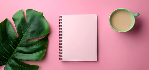 A serene workspace with a blank notepad, a cup of coffee, and a green leaf on a pink background, inviting creativity and relaxation.