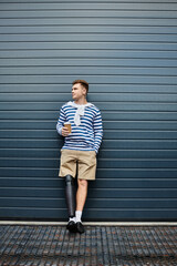 The young man stands confidently with a coffee cup, showcasing his prosthetic leg.