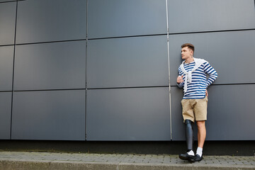 A young man leans against a wall, proudly showing off his prosthetic leg in daylight.