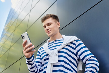 A stylish young man with a prosthetic leg enjoys using his smartphone against a sleek backdrop.