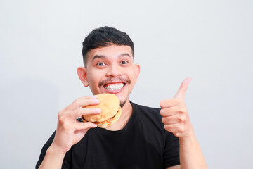 portrait of a young asian man is eating hamburger, isolated on white background. Fast food advertising