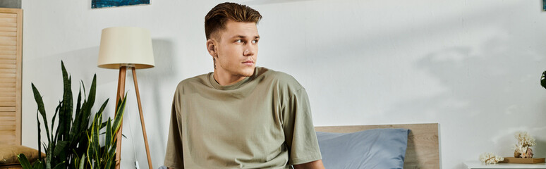 A young handsome man sits thoughtfully in a stylish bedroom, embracing his journey.