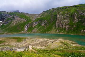 Male photographer taking pictures of beautiful mountain lanscape, small lake. Tourist on a trip, tripod photography, panorama. Grossglockner High Alpine Road. Austria