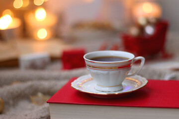 Various Christmas decorations, lit candles, cup of tea or coffee, cookies, books, presents and soft blanket on the table. Holiday hygge at home. Selective focus.