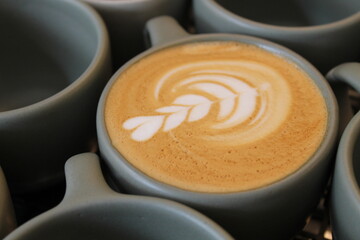 A coffee art close-up surrounded with more cups. A close-up shot of latte art on the surface of a coffee cup, such as a heart, leaf, or rosetta design