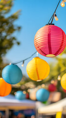 A row of colorful paper lanterns hangs beautifully against a bright blue sky, creating a festive atmosphere with shades of pink, yellow, and blue