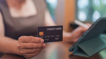 A woman is holding a credit card in her hand. She is sitting at a table with a tablet in front of her